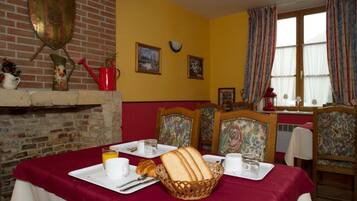A dining area with a brick fireplace, yellow walls, floral chairs, and a table set with bread, plates, and glasses.
