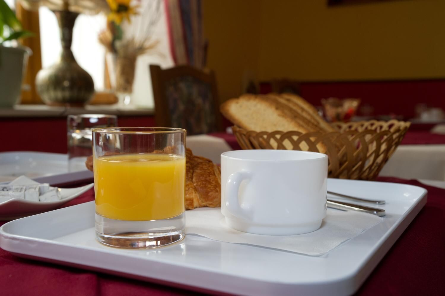 A breakfast tray with a glass of orange juice, a white mug, and a croissant on a white tray.