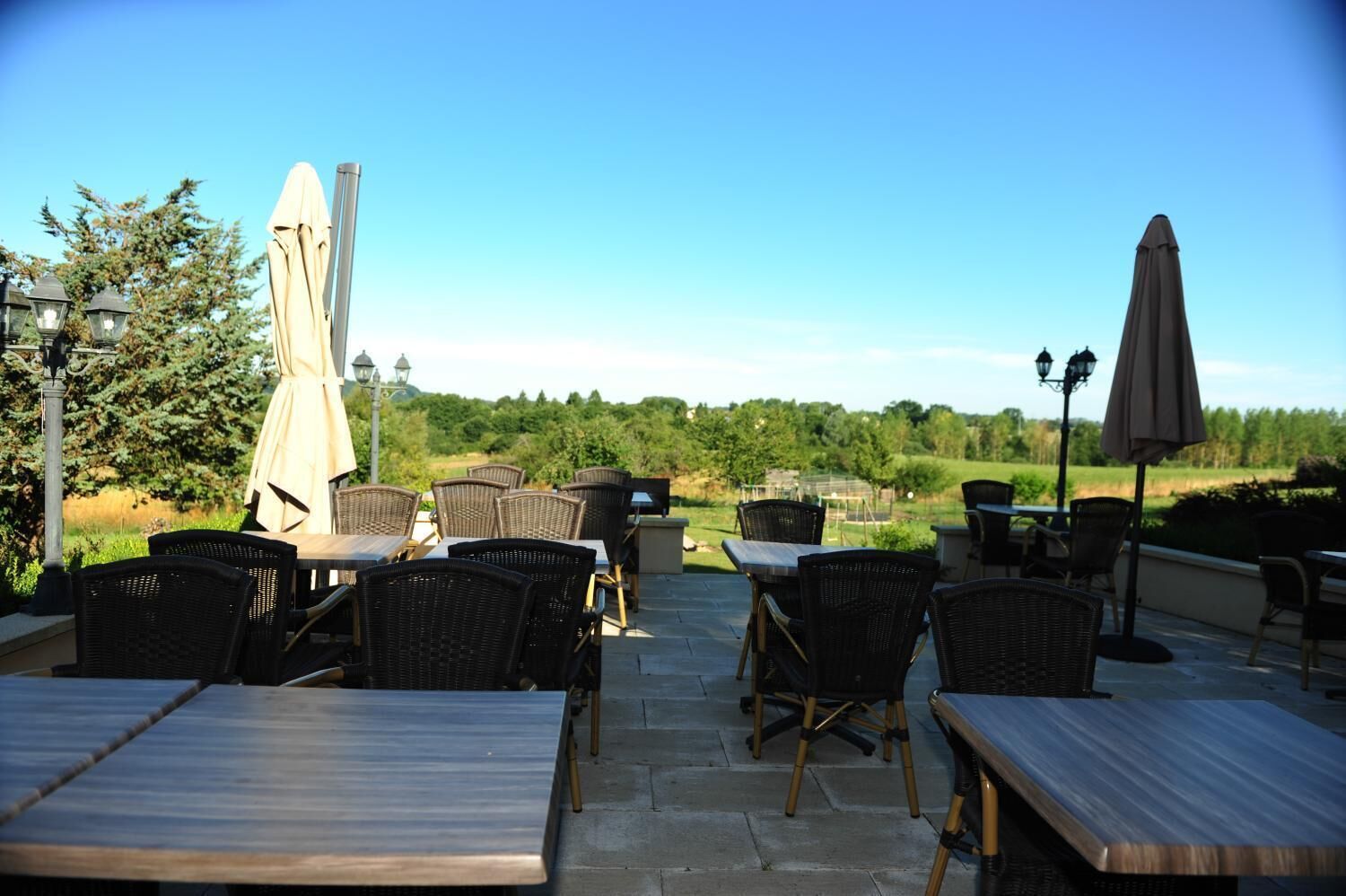 Une terrasse extérieure aménagée avec des meubles en osier et des parasols, offrant une vue sur un paysage verdoyant.