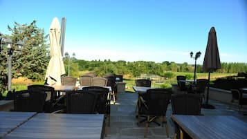 Une terrasse extérieure aménagée avec des meubles en osier et des parasols, offrant une vue sur un paysage verdoyant.