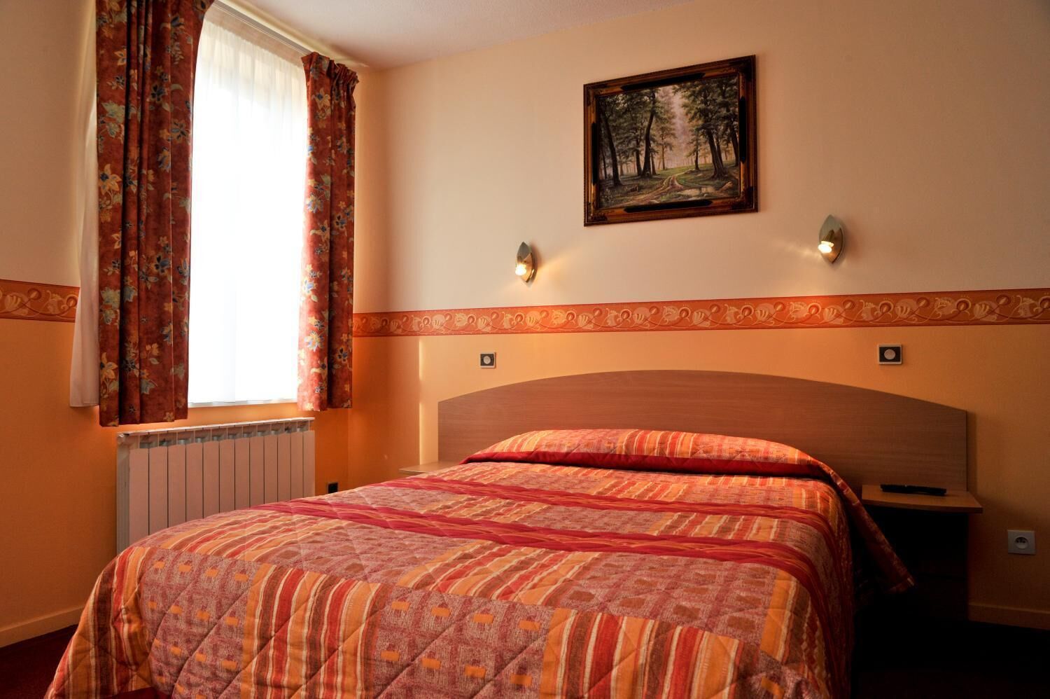 Une chambre avec un grand lit, des rideaux à motifs floraux, un tableau au mur et un radiateur.