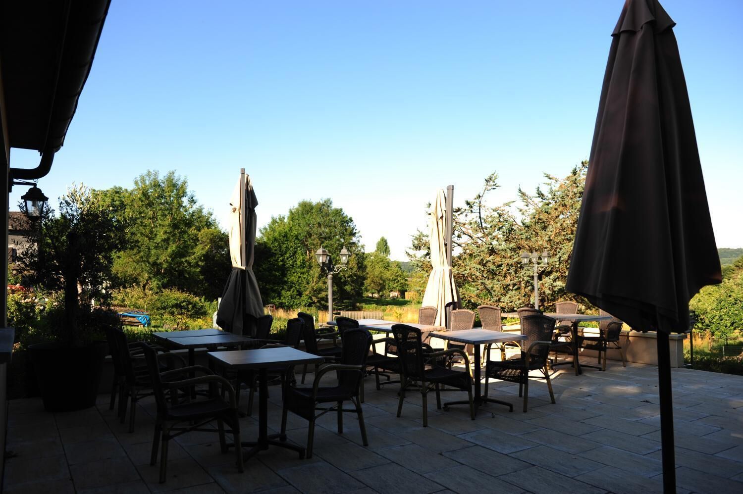 An outdoor patio with tables and chairs, surrounded by trees and a clear sky.