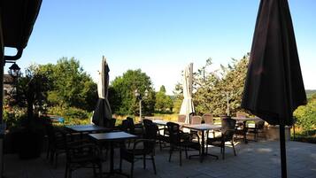 An outdoor patio with tables and chairs, surrounded by trees and a clear sky.