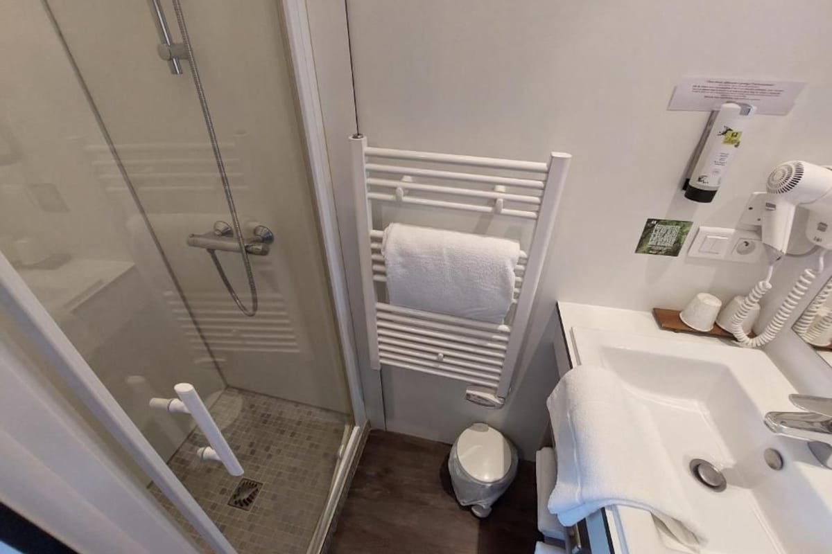 A bathroom with a glass shower enclosure, a white towel rack, a toilet, and a sink with a mirror.