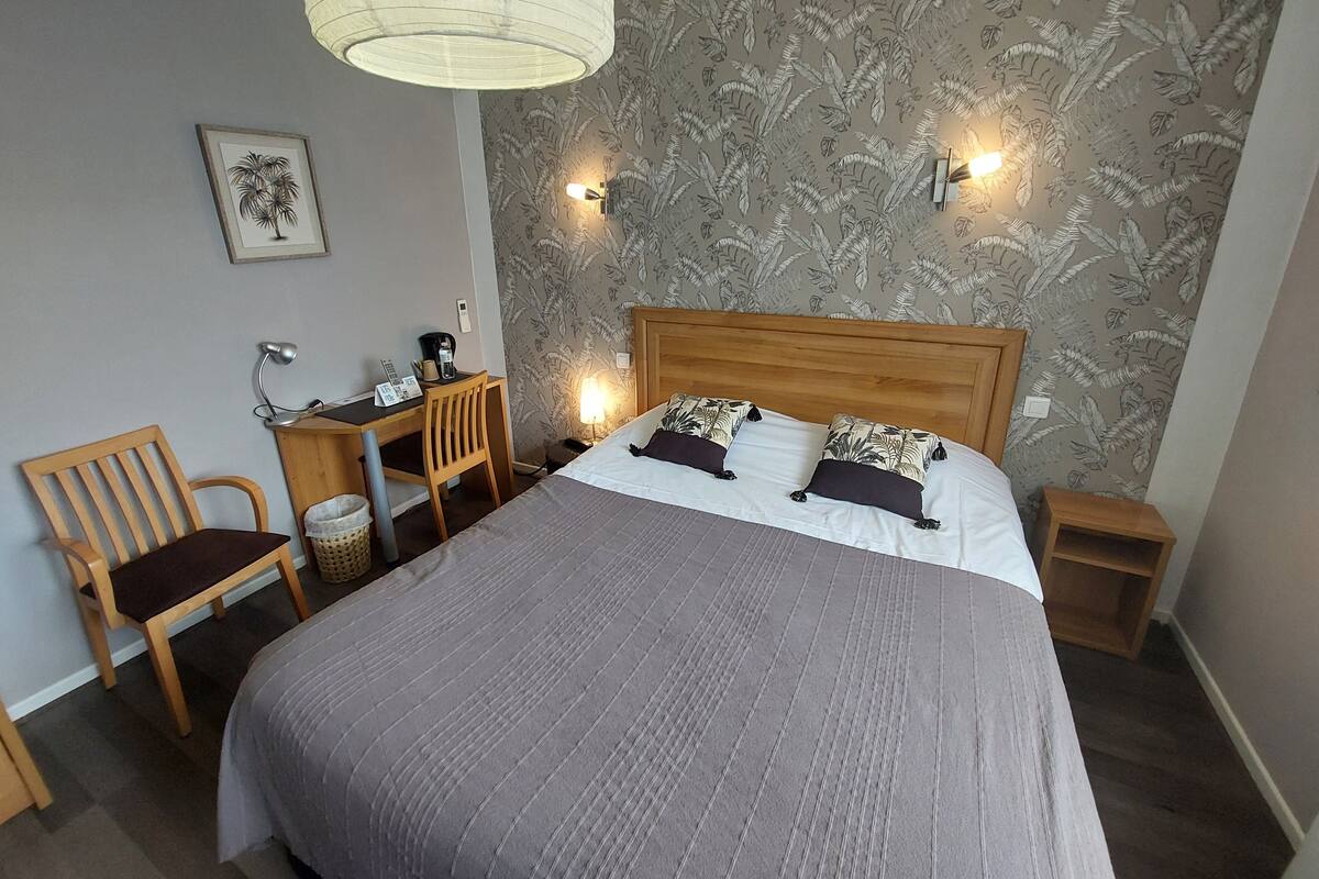 Habitación de hotel con cama, escritorio, silla, lámpara y un muro con diseño de hojas.