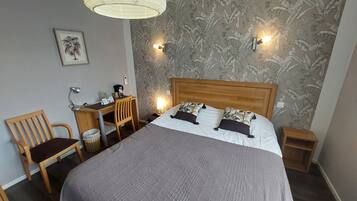 A hotel room with a bed, a desk, a chair, a lamp, and a wall with a leaf pattern.