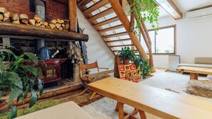 A cozy living room with a fireplace, wooden beams, a dining table, and potted plants. - Country Inn Milky House (Niseko)