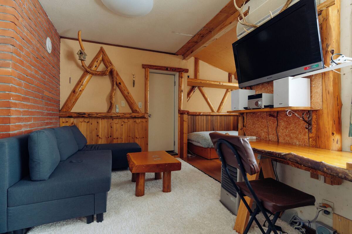 Une pièce confortable avec un canapé, une table en bois, un téléviseur fixé au mur et un lit.