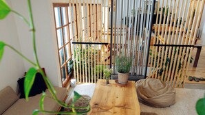 A room with a wooden table, a sofa, and a view through a bamboo screen to a balcony with plants and shoes. - Country Inn Milky House (Niseko)