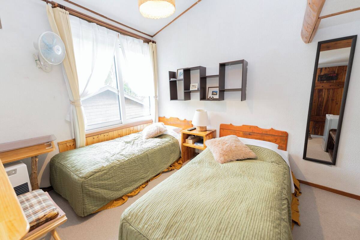 Une chambre avec deux lits simples, une table de chevet avec une lampe, un miroir et une fenêtre avec des rideaux.