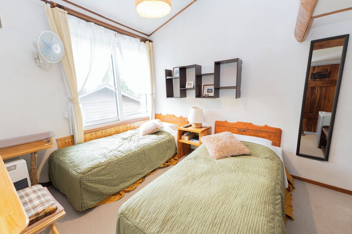 Una habitación con dos camas individuales, una mesita de noche con lámpara, un espejo y una ventana con cortinas.
