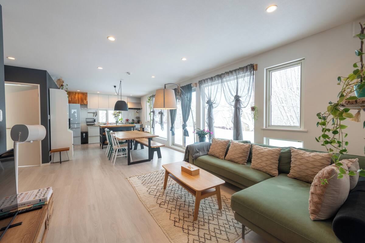 A modern living room with a green sofa, wooden coffee table, and a dining area with a table and chairs.