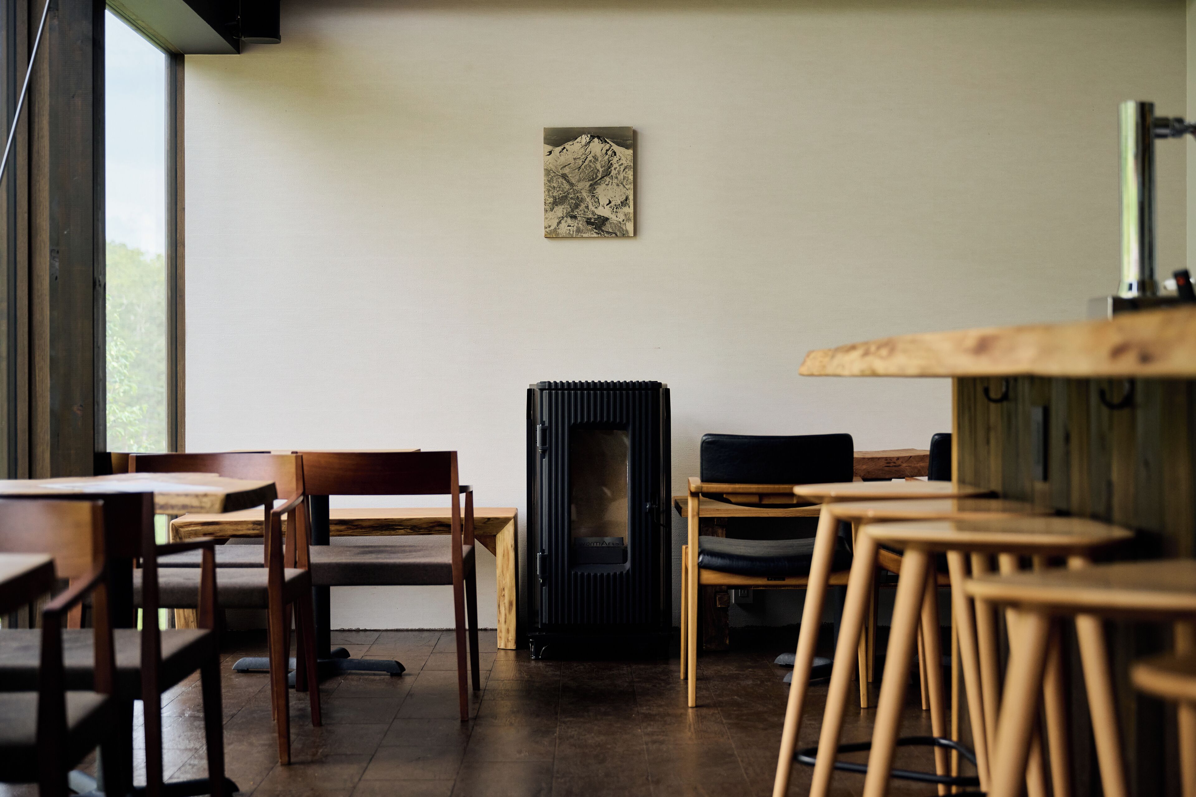 A cozy room with wooden furniture, a black wood stove, and a mountain painting on the wall.