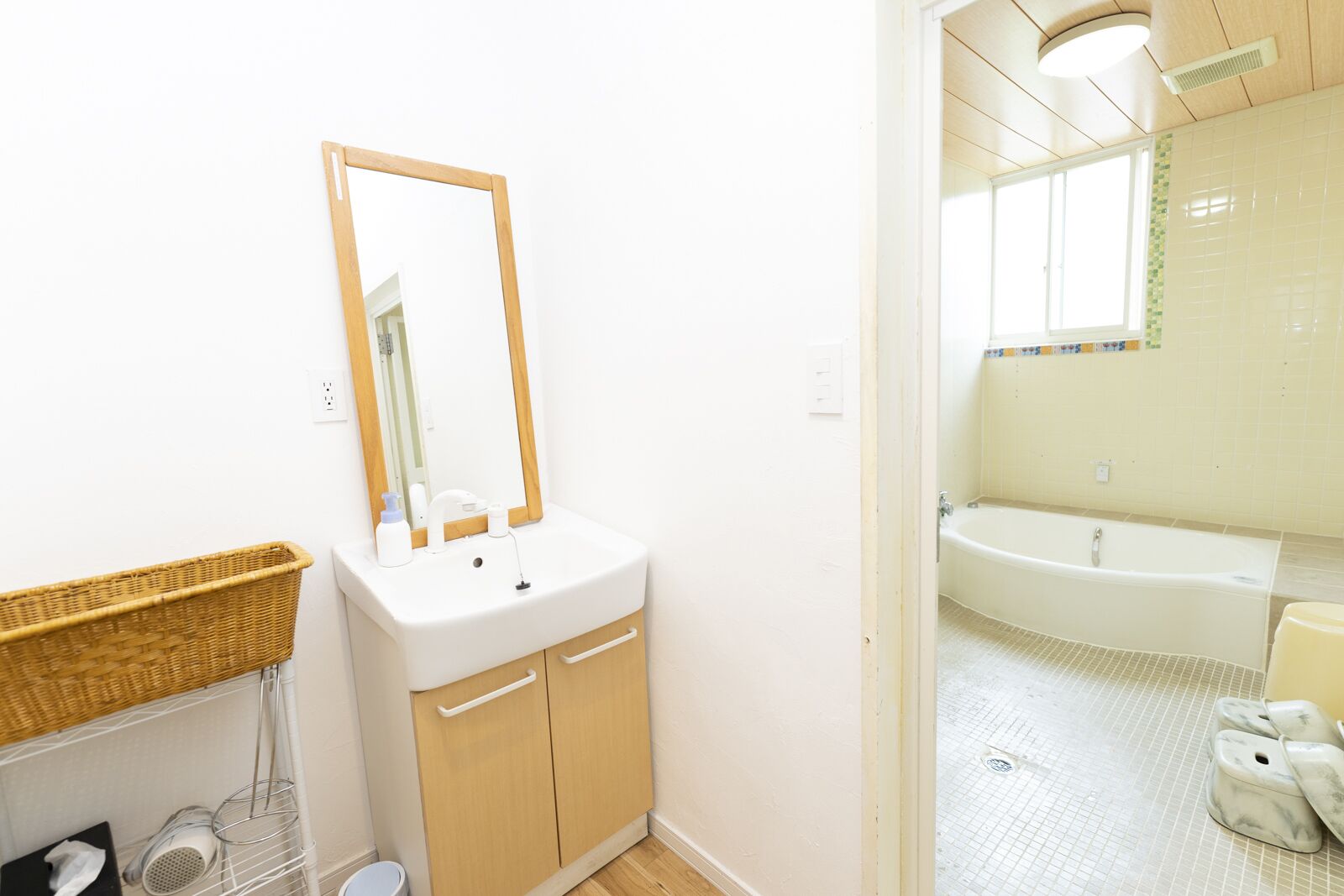 A bathroom with a white sink, wooden cabinets, a mirror, a bathtub, and a wicker basket.