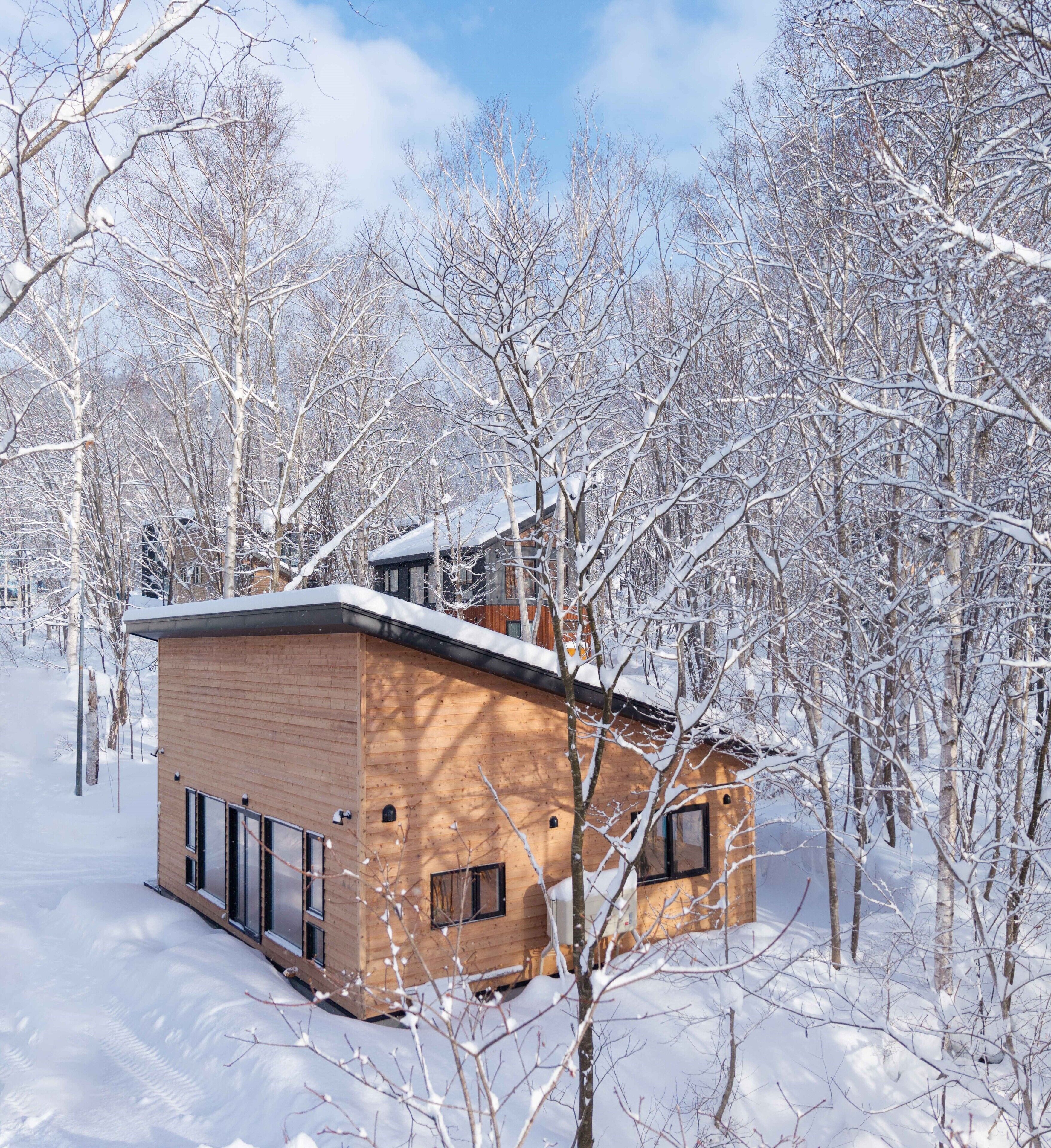 A wooden cabin with a sloped roof, surrounded by snow-covered trees.