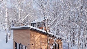 A wooden cabin with a sloped roof, surrounded by snow-covered trees.