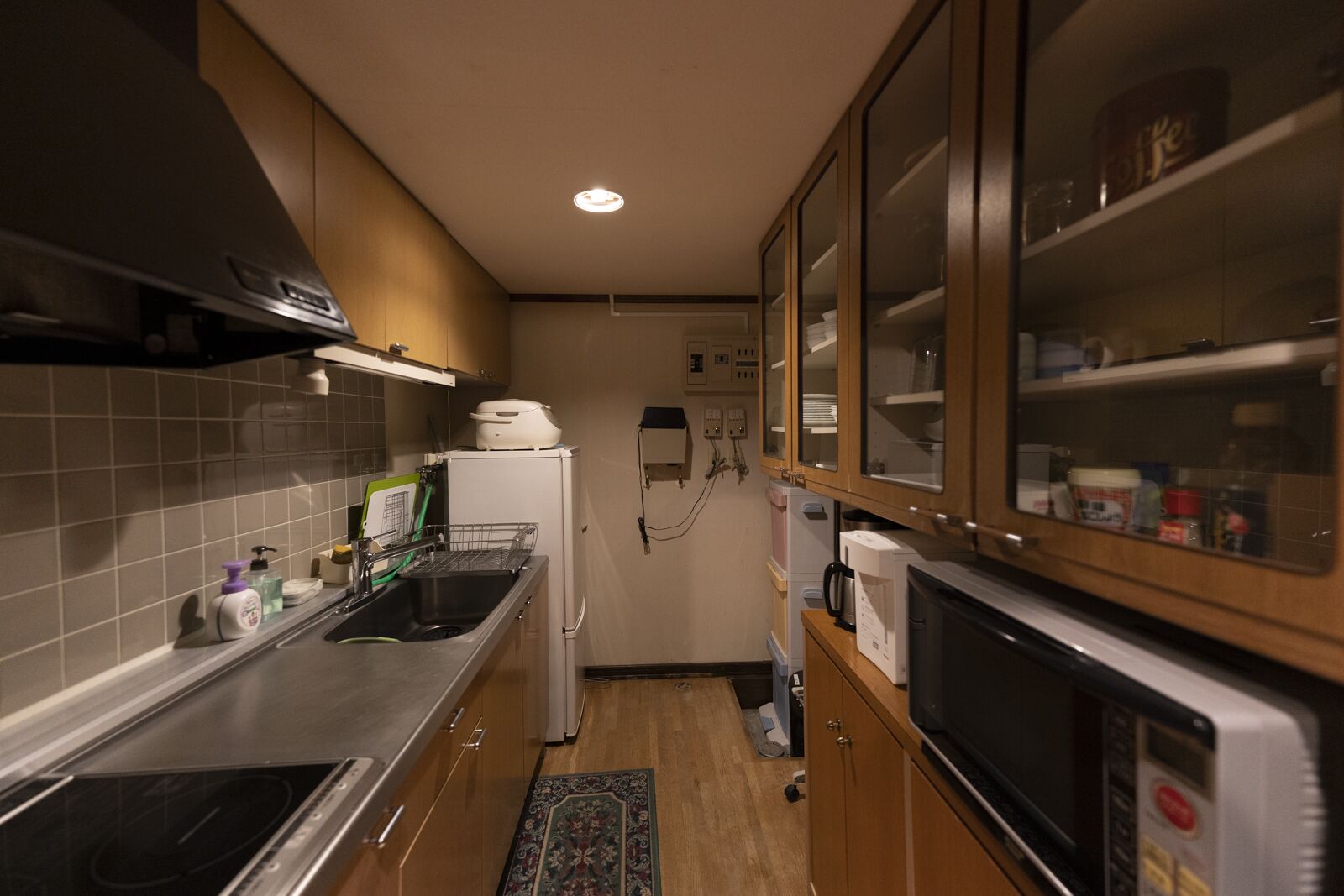 A compact kitchen with a stove, sink, and microwave. There are cabinets with glass doors and a small refrigerator.