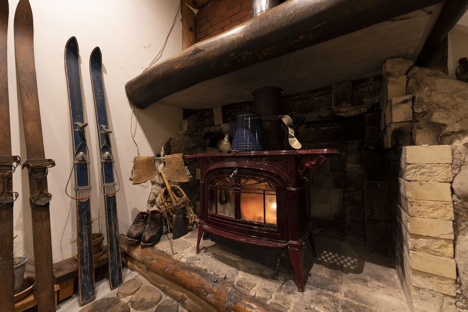 Una habitación rústica con chimenea de piedra, esquíes apoyados en la pared y un estufa de leña.