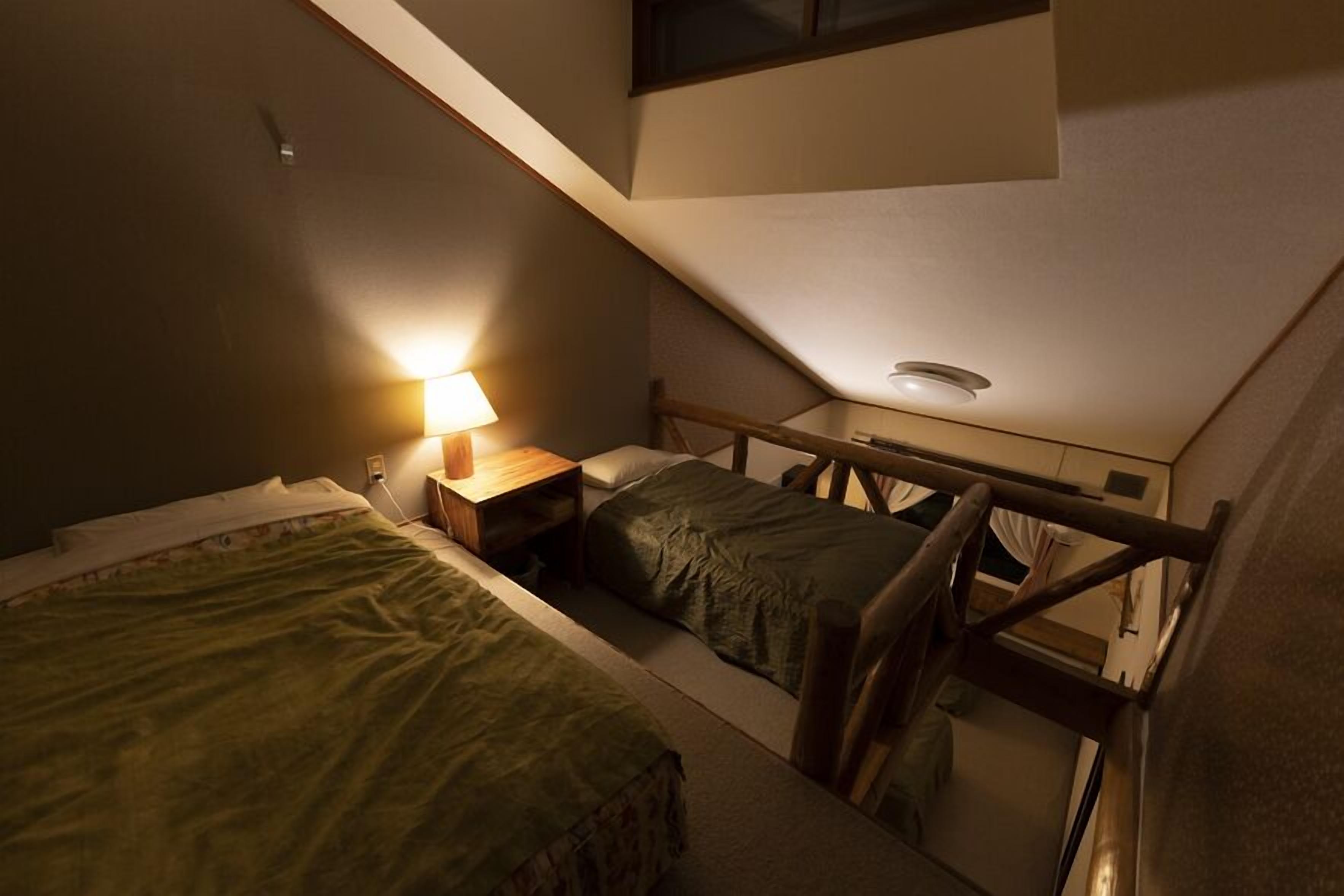 A small, dimly lit room with two beds, a nightstand, and a staircase.