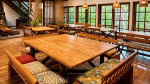 A spacious dining area with wooden tables and benches, large windows with a view of greenery, and a staircase leading to an upper level. - Country Inn Milky House (Niseko)