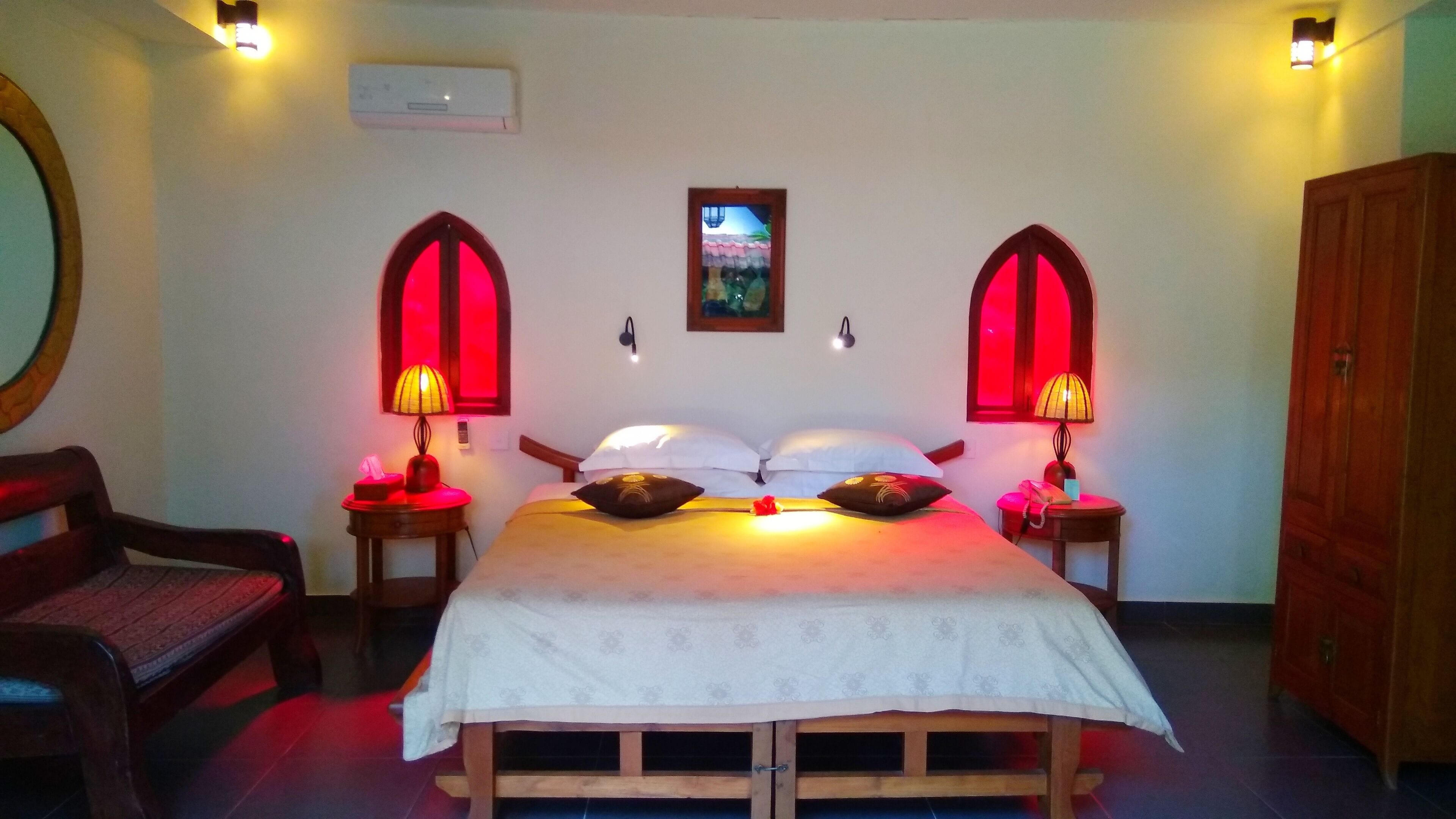Un dormitorio con cama, dos mesitas de noche con lámparas, una silla, armario y aire acondicionado.