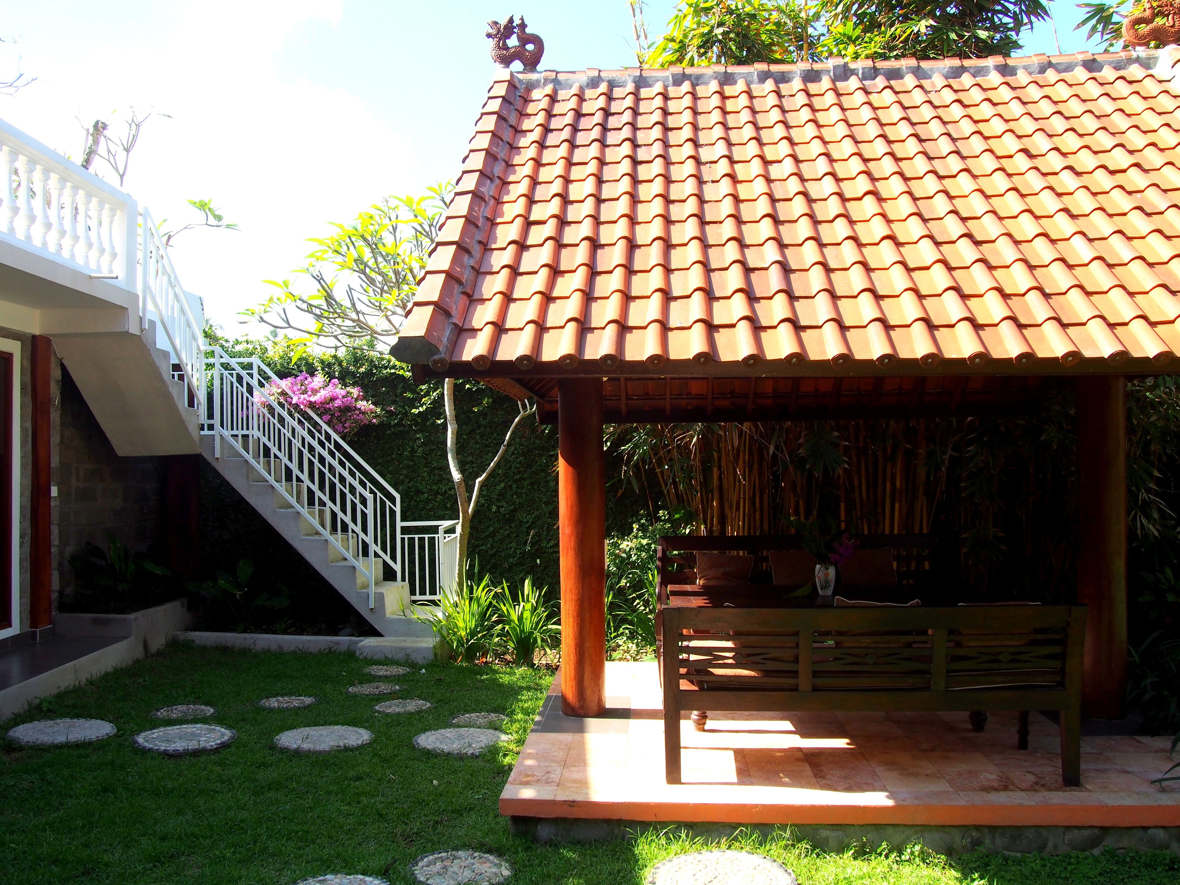 A traditional gazebo with a tiled roof, a wooden bench, and a staircase leading to a white balcony.