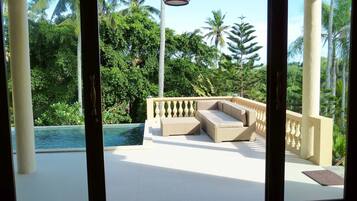 Un balcón con piscina, mobiliario exterior y exuberante vegetación.