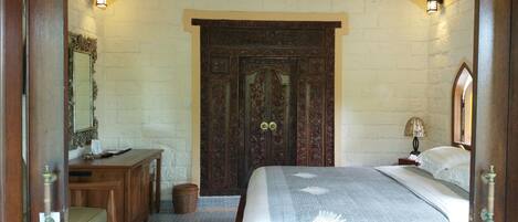 Un dormitorio con una cama grande, un aparador de madera, un espejo y una puerta con detalles tallados.