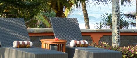 Two lounge chairs with cushions, a small round table, and a view of the ocean.