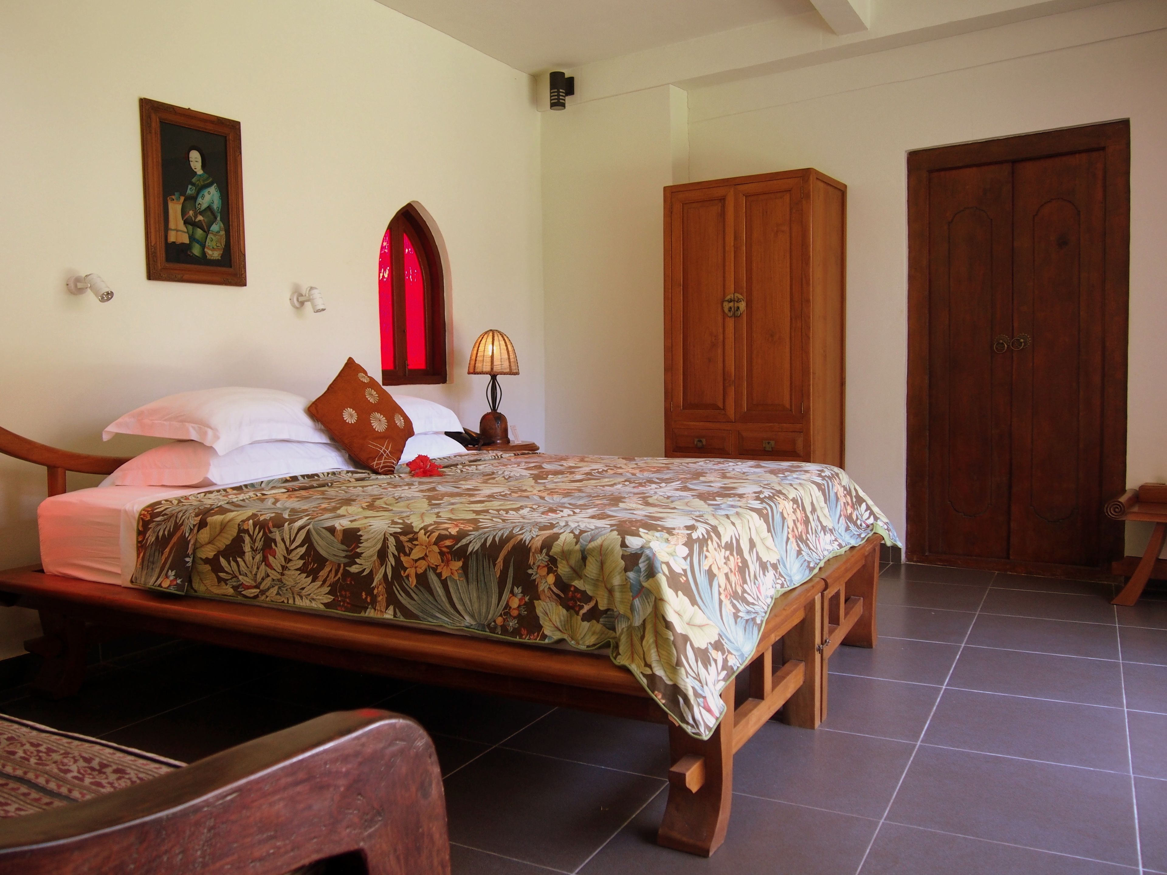 A bedroom with a wooden bed, a nightstand with a lamp, a wardrobe, and a door.