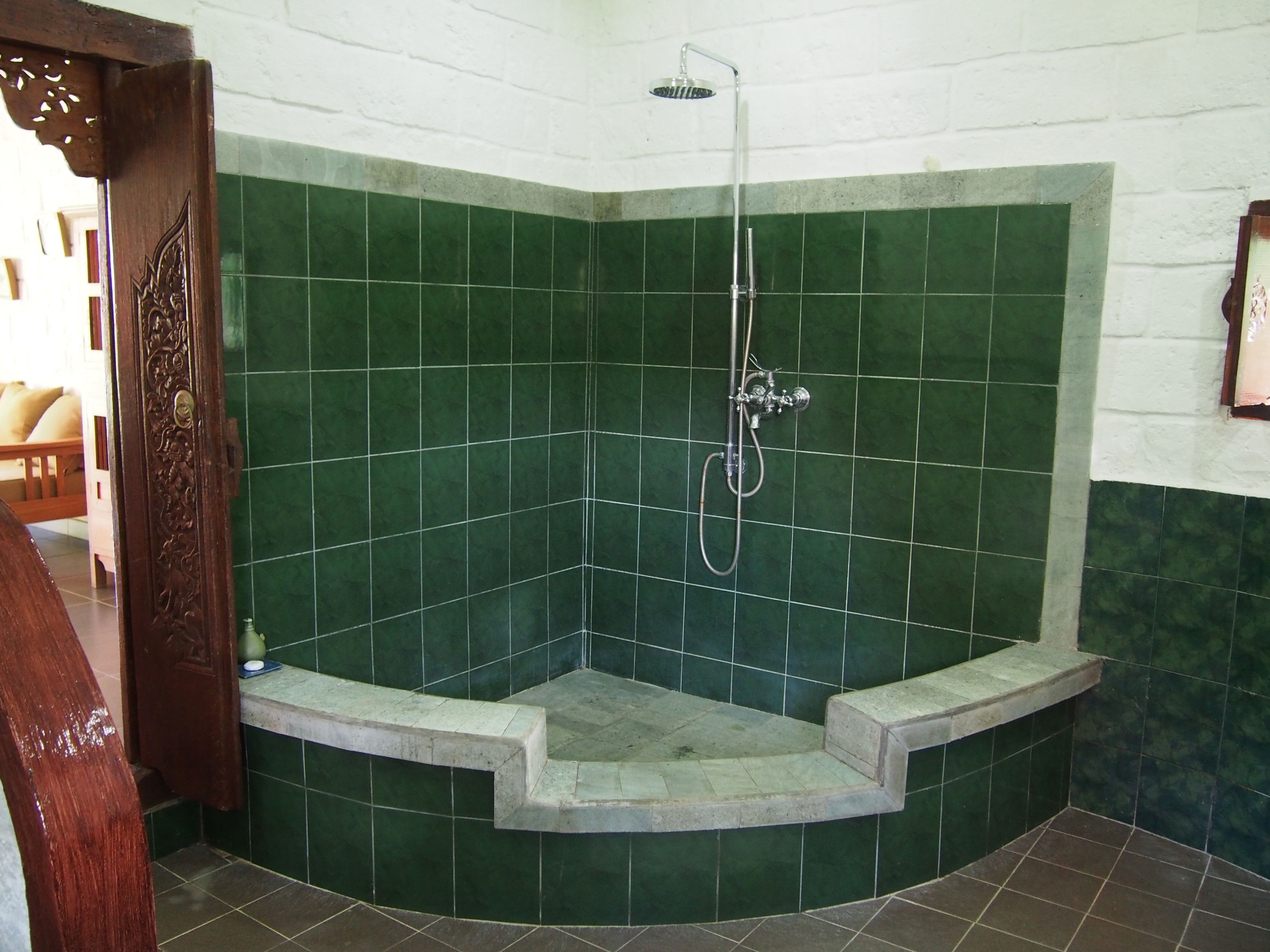 Ducha en esquina con azulejos verdes y un marco de puerta de madera.