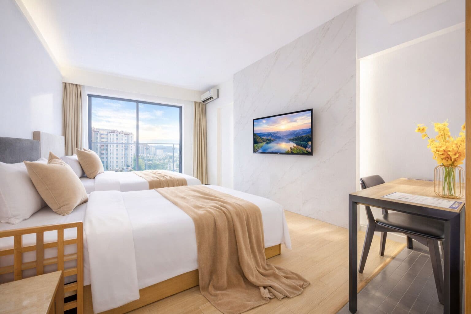 A hotel room with two beds, a desk, a chair, a TV, and a window with a city view.