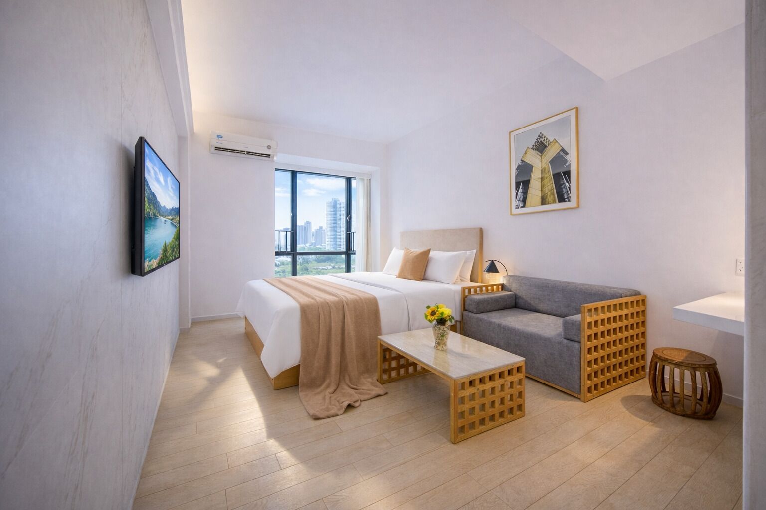 A hotel room with a bed, a sofa, a coffee table, a small stool, a picture on the wall, and an air conditioning unit.