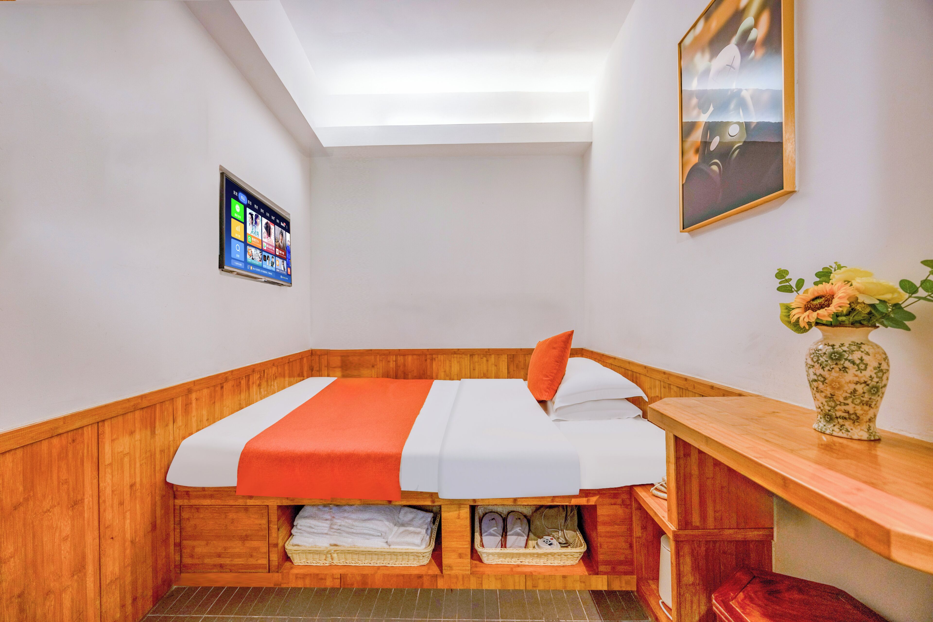 Habitación de esquina con cama, banca de madera y televisor instalado en la pared.