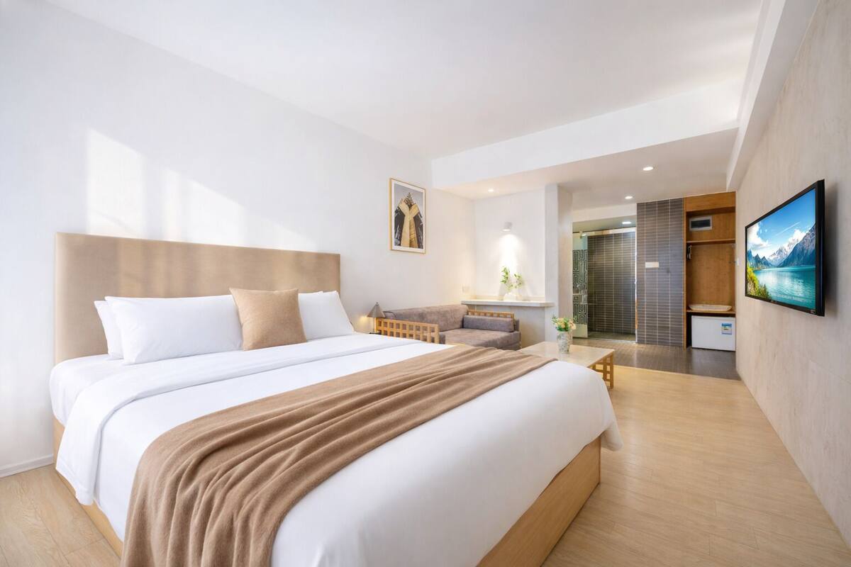A modern hotel room with a large bed, a sofa, a TV, and a shower area.