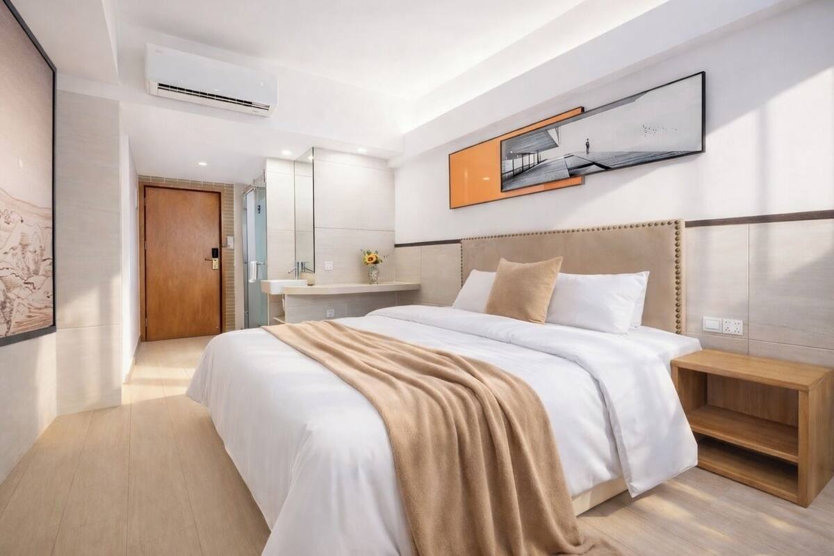 A modern hotel room with a large bed, a bedside table, a mirror, and a wall-mounted artwork.