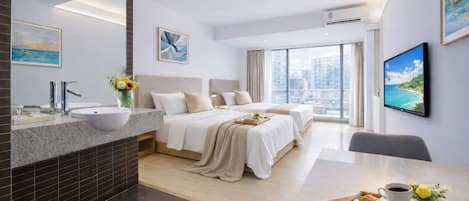 A modern hotel room with a large bed, a separate seating area, a bathroom with a sink, and a city view.