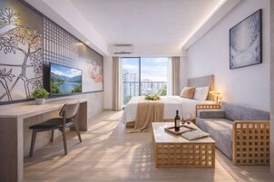 Una camera d'albergo moderna con un letto grande, una scrivania con una sedia, un divano e un tavolino. Si vede una finestra con vista sugli edifici e un quadro appeso al muro.