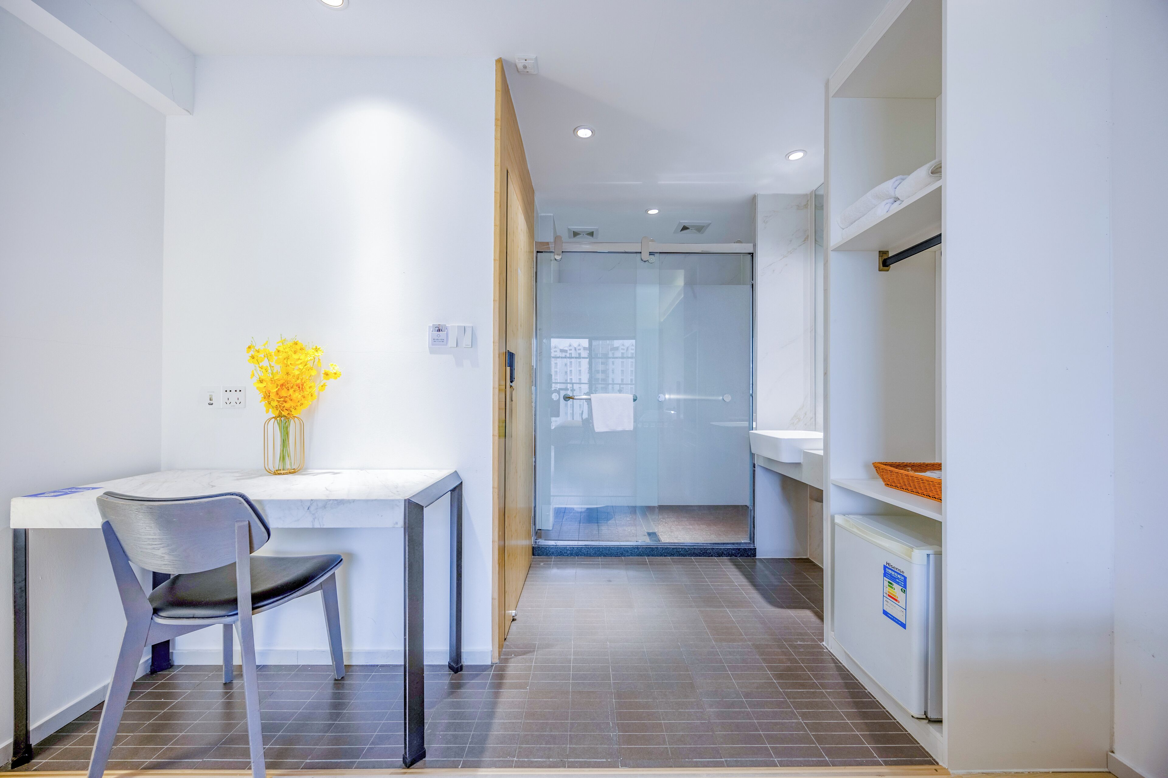 A modern bathroom with a glass shower enclosure, a white sink, and a small refrigerator.