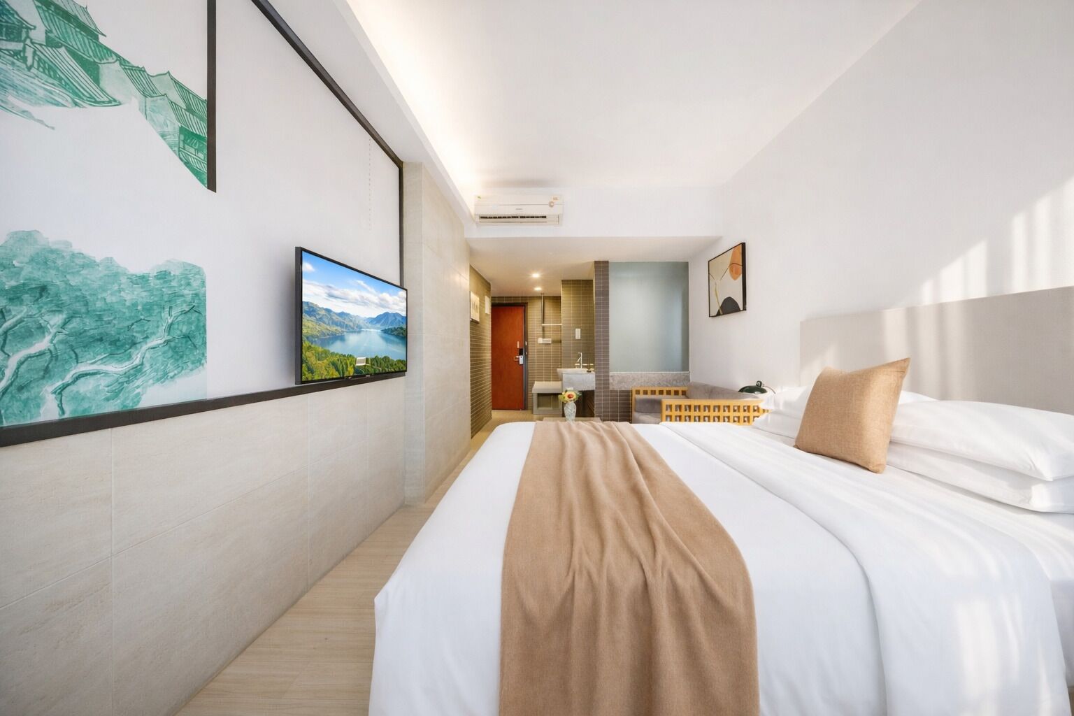 A hotel room with a large bed, a TV, artwork on the walls, and a bathroom visible in the background.