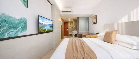 A hotel room with a large bed, a TV, artwork on the walls, and a bathroom visible in the background.