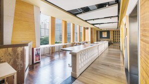 Un interior moderno con una larga barra, zona de estar y ventanas amplias que ofrecen vistas de edificios.