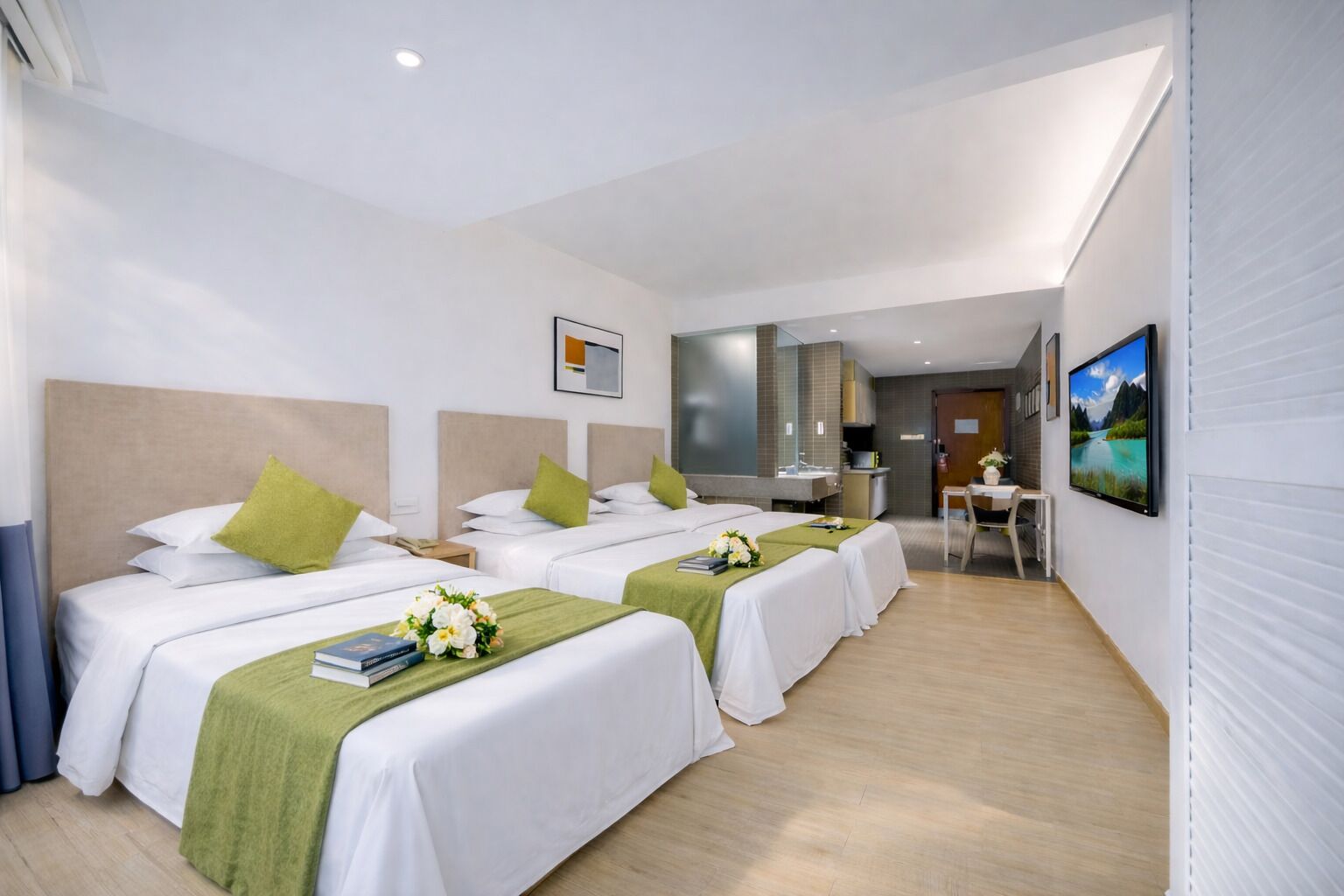 A hotel room with three beds, a desk, a TV, and a bathroom.