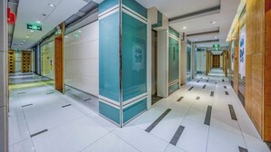 Un pasillo moderno de hotel con divisiones de vidrio, paneles de madera y piso de baldosas.