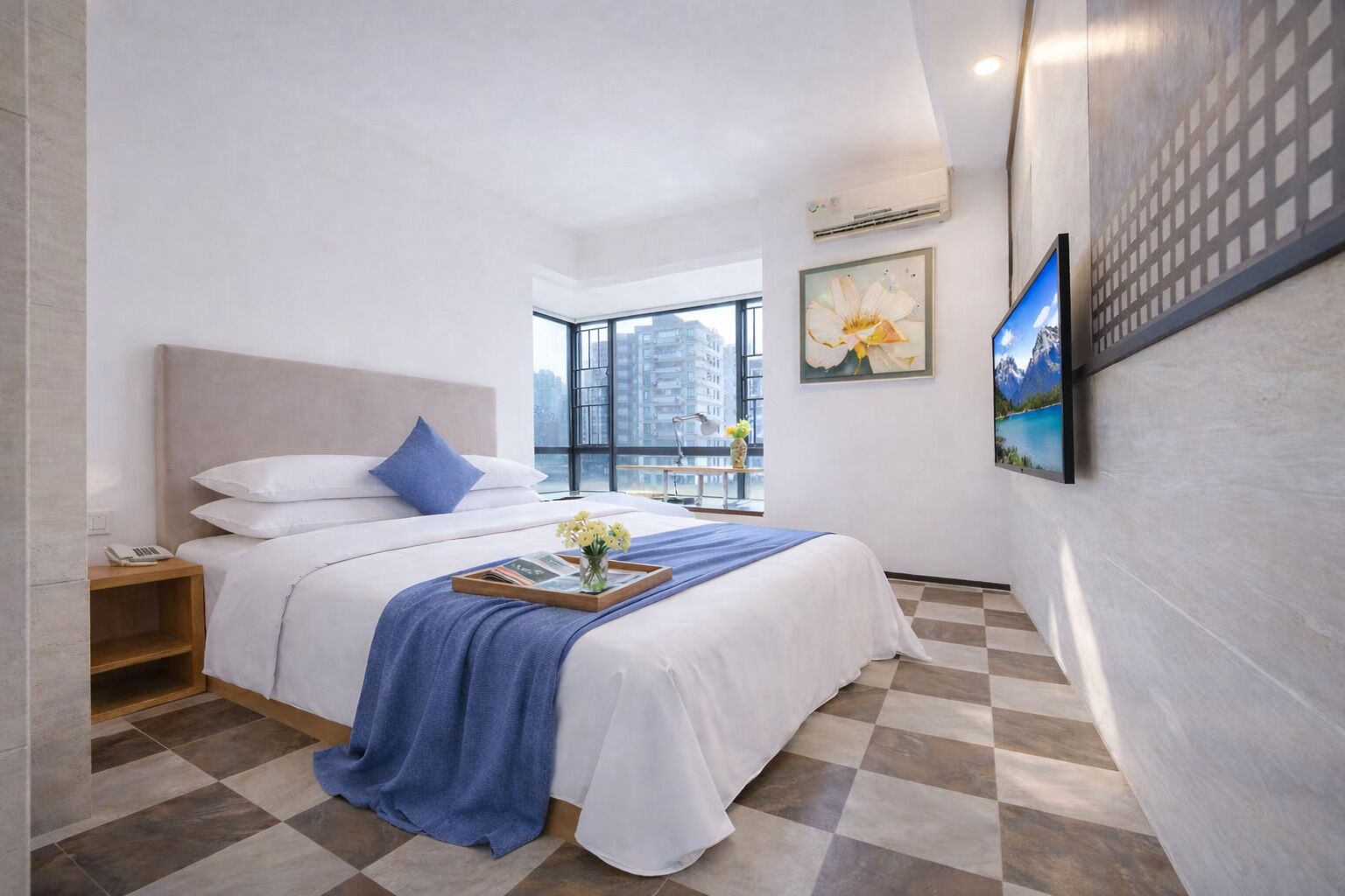 A hotel room with a large bed, a nightstand, a window with a city view, and a mounted painting.