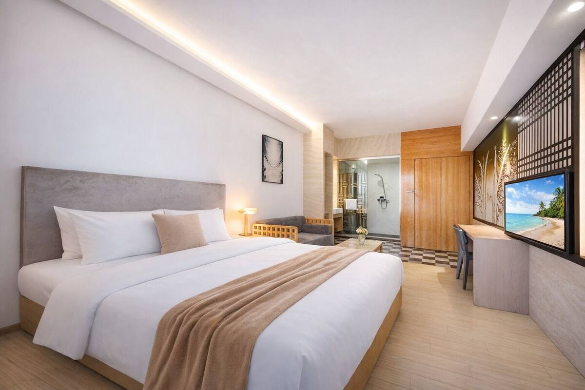 A modern hotel room with a large bed, a desk, a shower, and a TV displaying a beach scene.