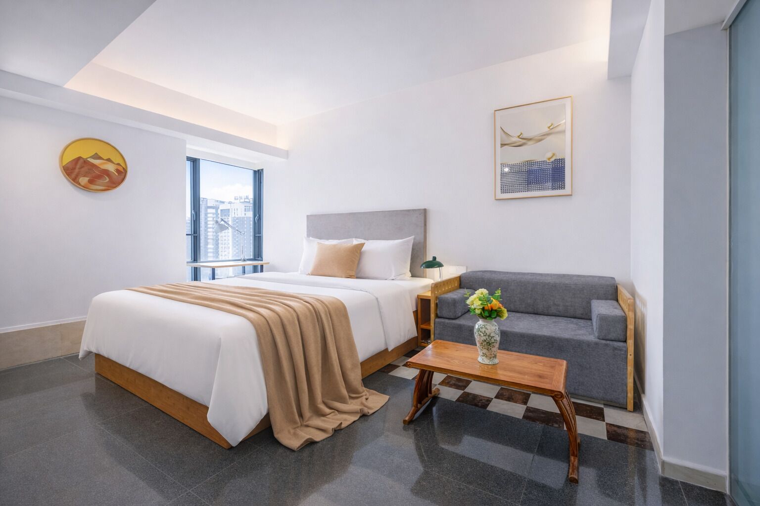 A modern hotel room with a bed, a sofa, a coffee table, and a window with a city view.