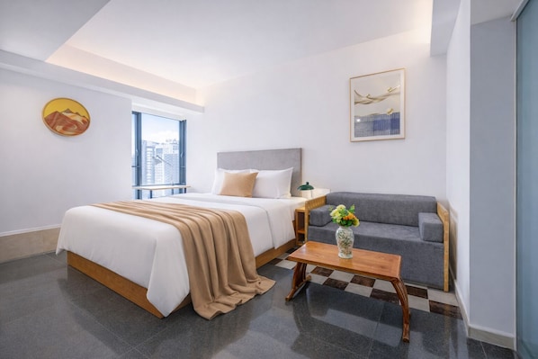 A modern hotel room with a bed, a sofa, a coffee table, and a window with a city view. - Timmy Hotel (Guangzhou)