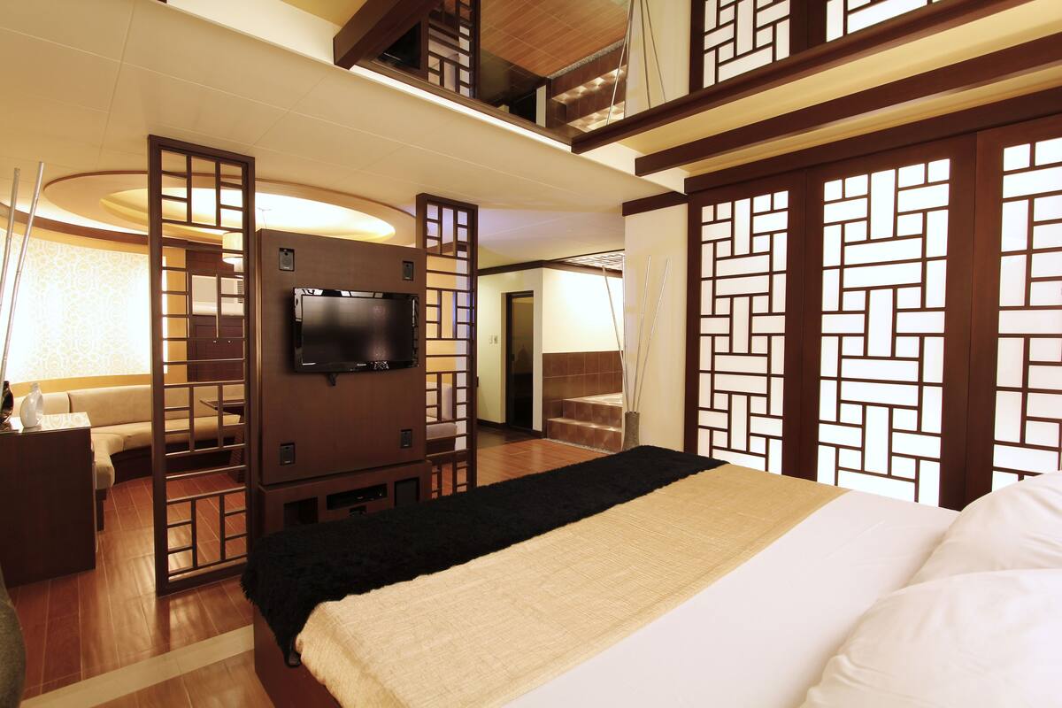 Una camera d'albergo con un letto, una televisione, un pannello di legno e una scala.