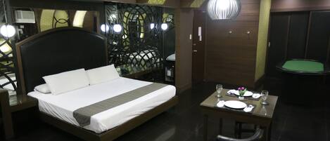 A modern hotel room with a large bed, a dining table with chairs, and a green pool table.